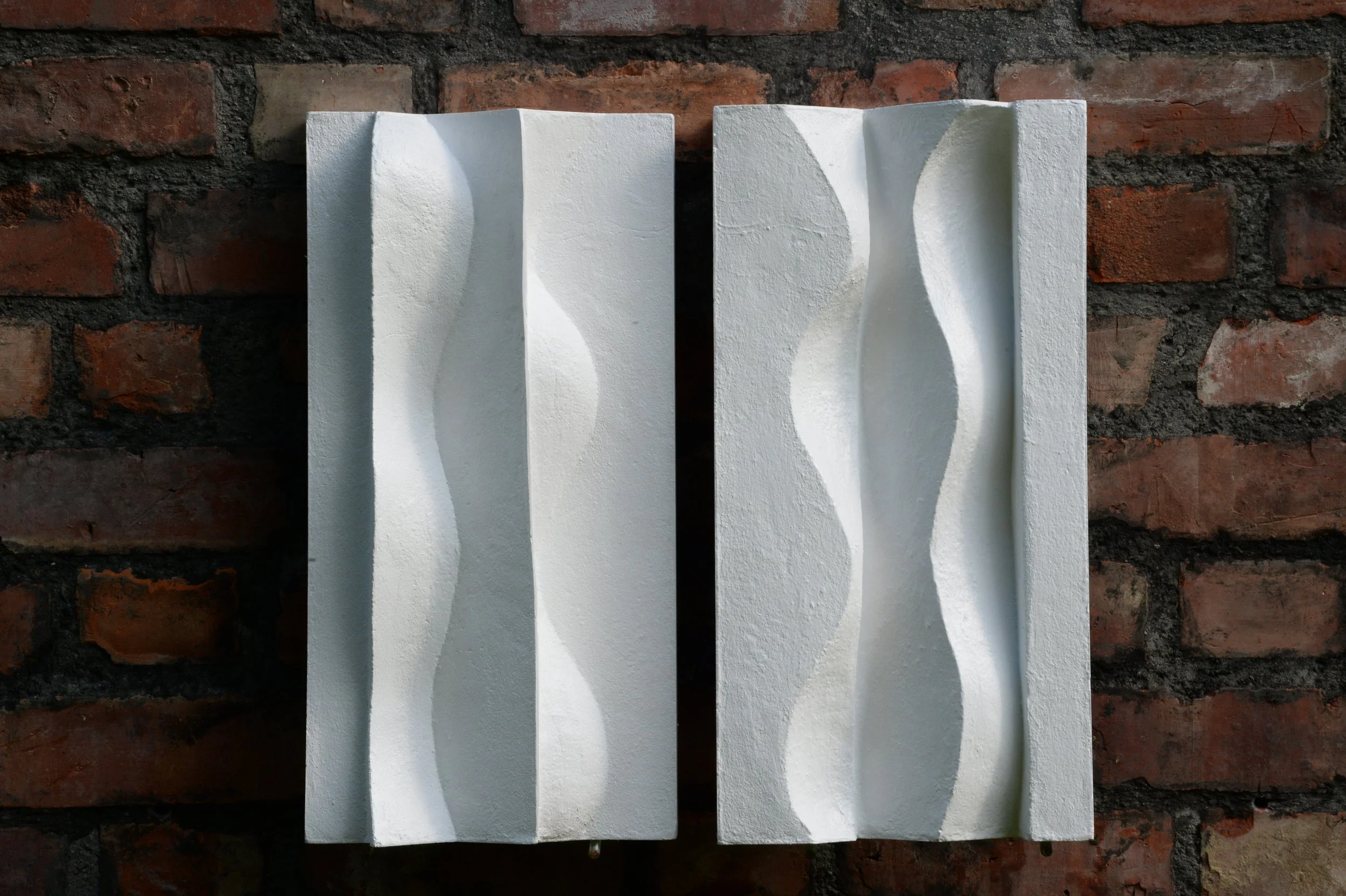 Paired white Brancusi panels on brick, with broad shadows along the flowing vertical relief.