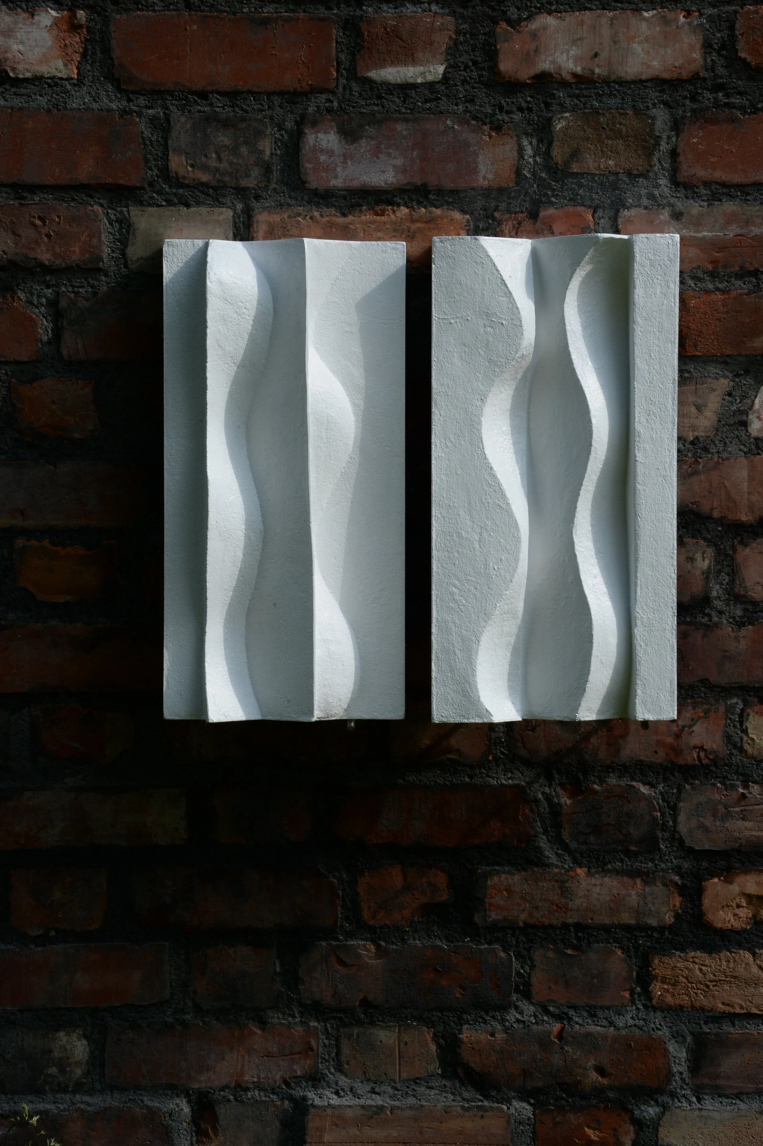 Paired white Brancusi relief panels on dark brick, with shadows defining the vertical curves.