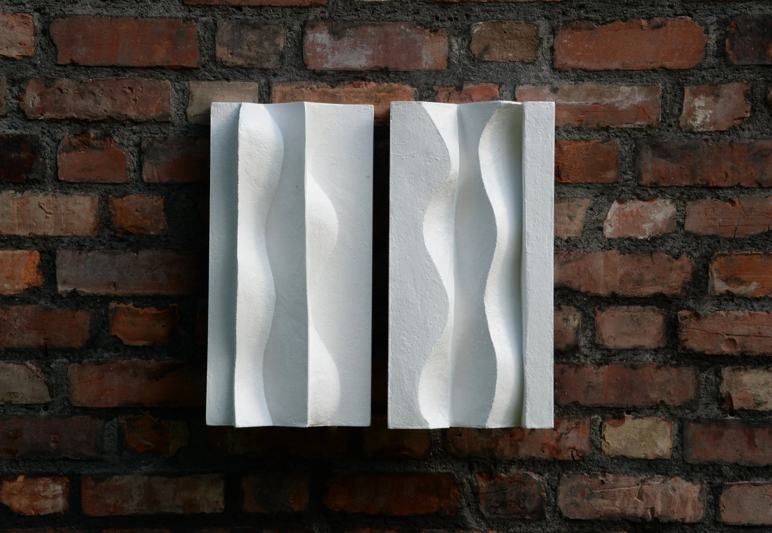 Two white Brancusi panels on brick, with alternating raised and recessed curves.