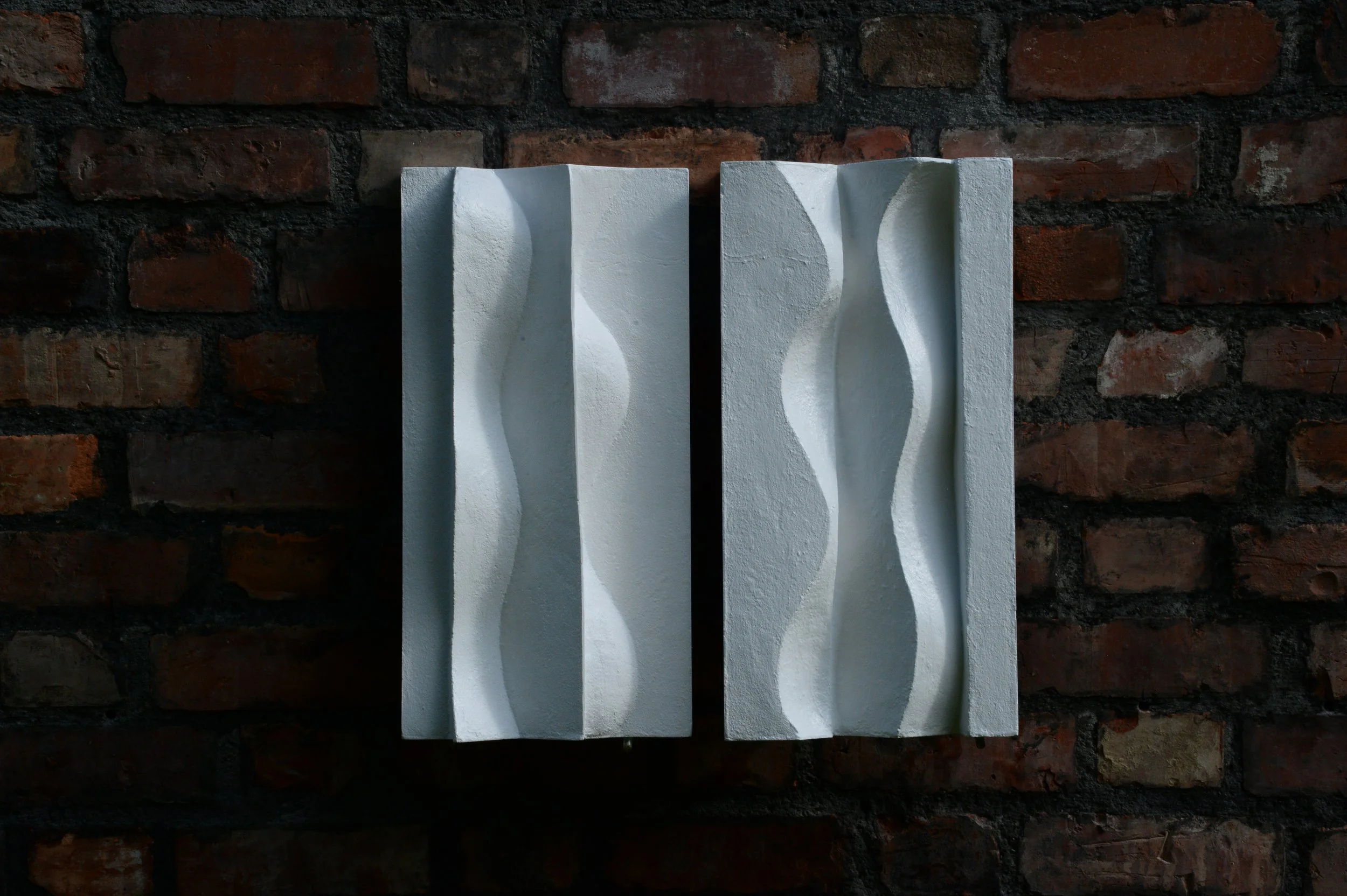 Two white Brancusi panels on a brick wall, with their flowing relief forms shown side by side.