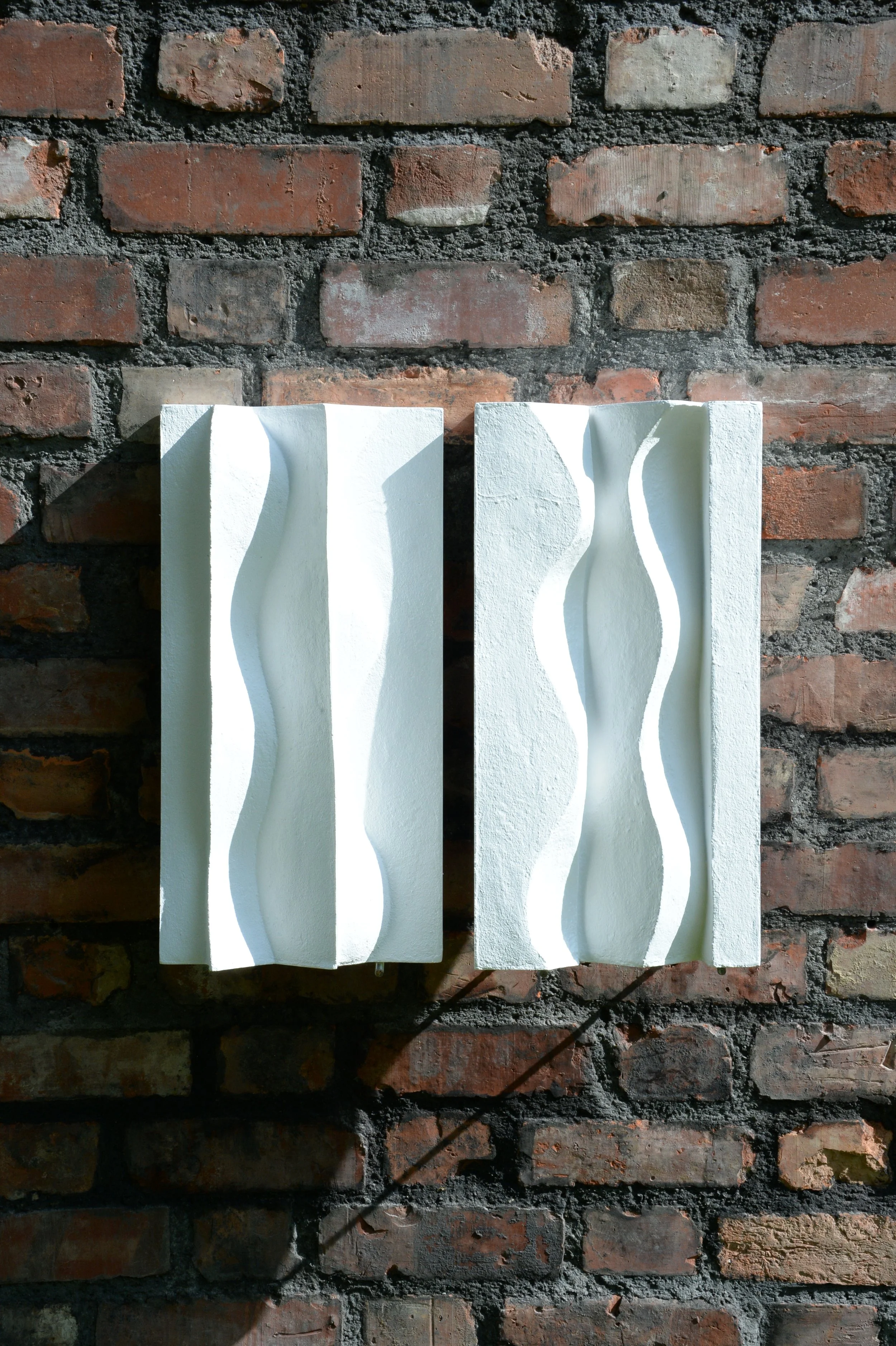 Two tall white Brancusi relief panels with flowing vertical curves, displayed on brick.