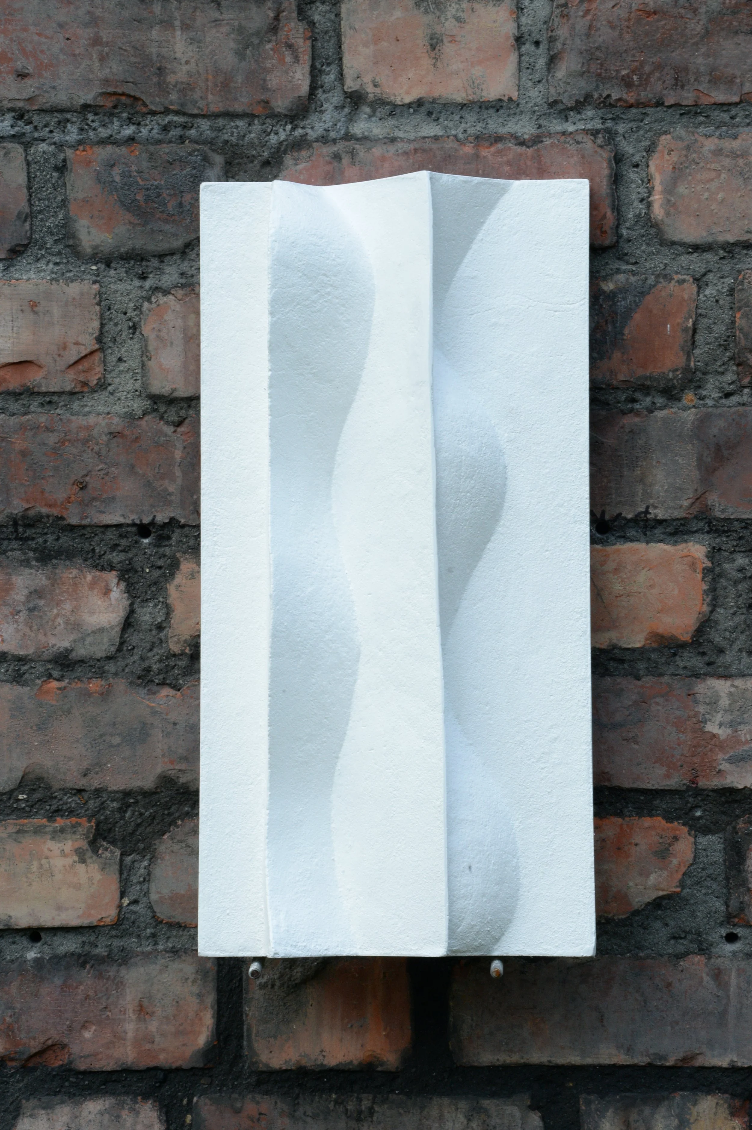 White Brancusi 2 relief mounted vertically on brick.