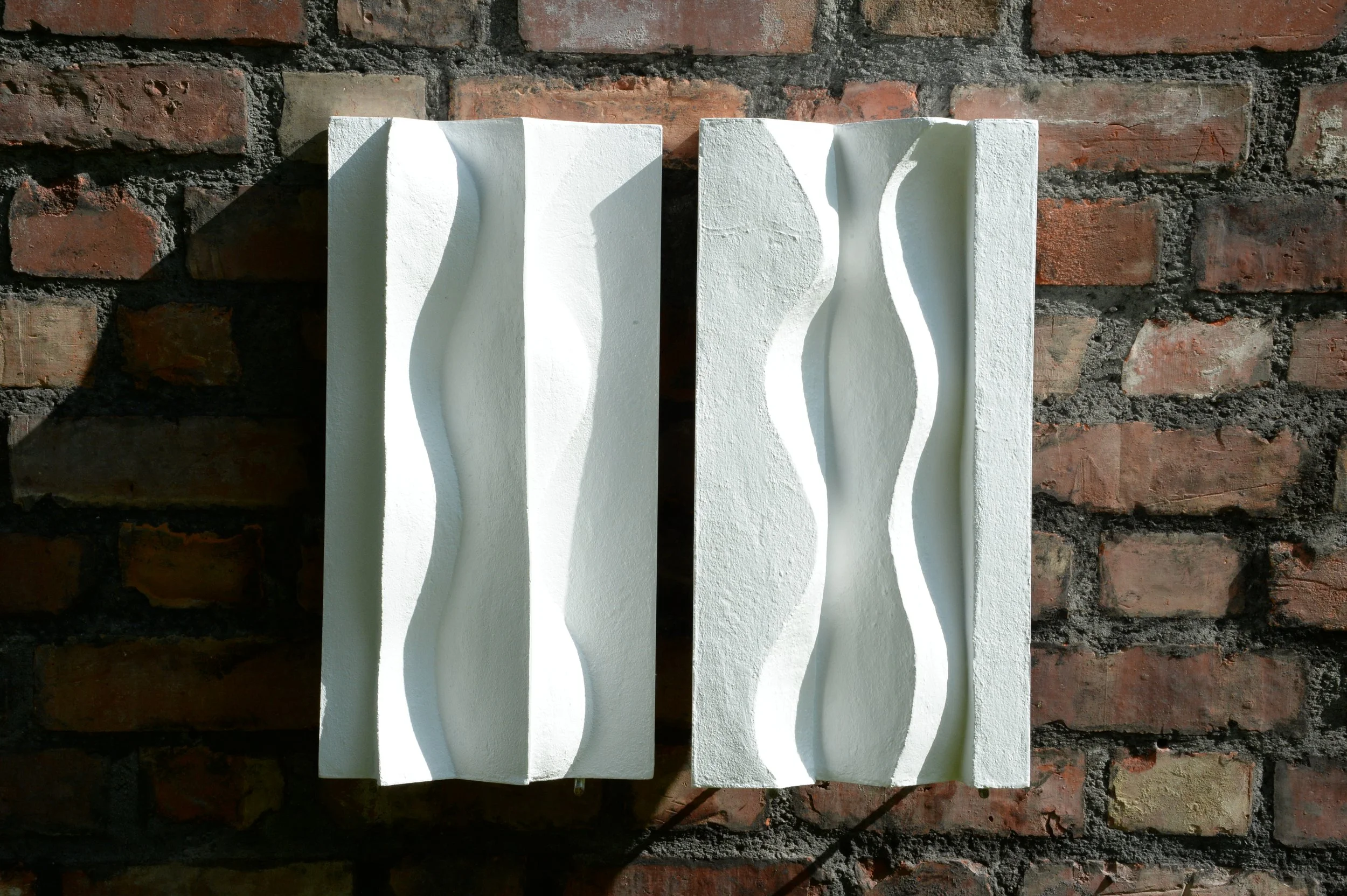 Front view of paired white Brancusi panels, with contrasting raised and recessed wavy forms.