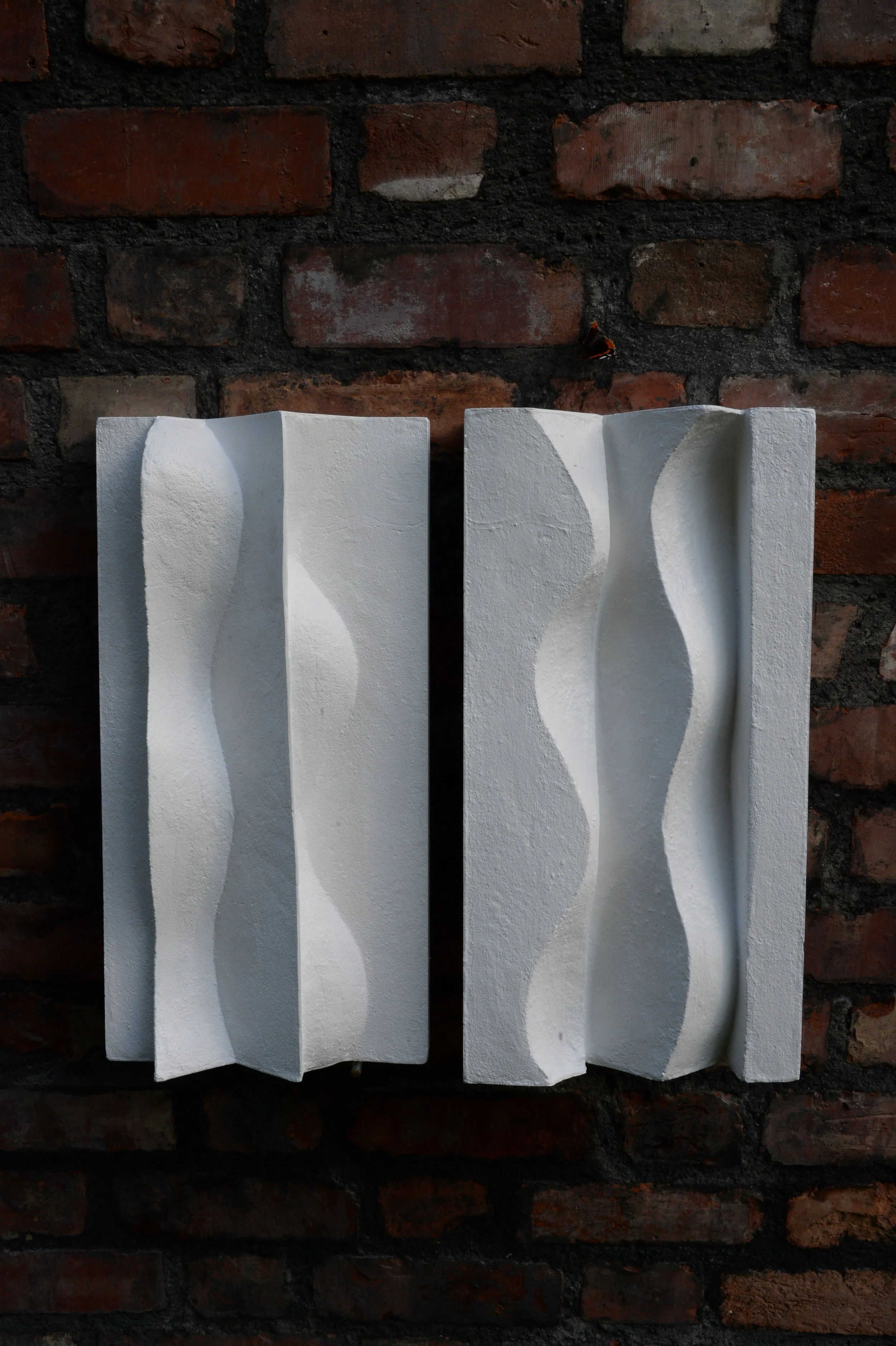Angled view of the paired white Brancusi relief panels on a brick wall.