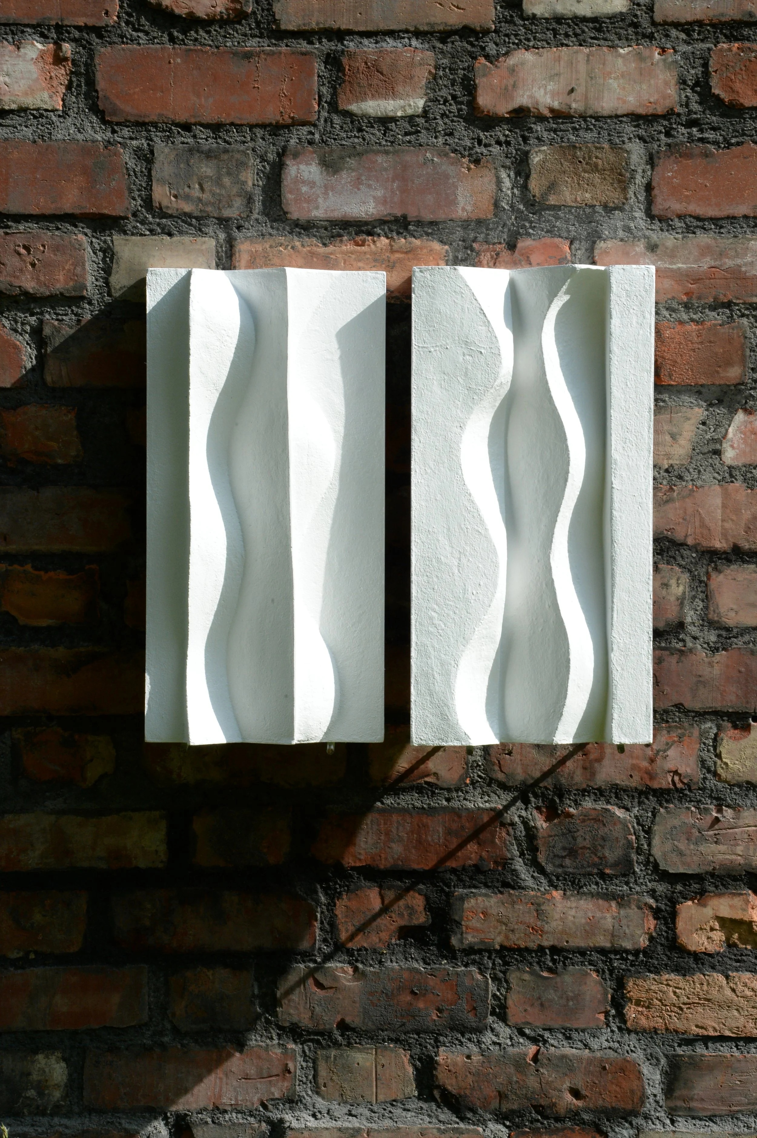 White Brancusi diptych on a brick wall, showing both tall curved panels.