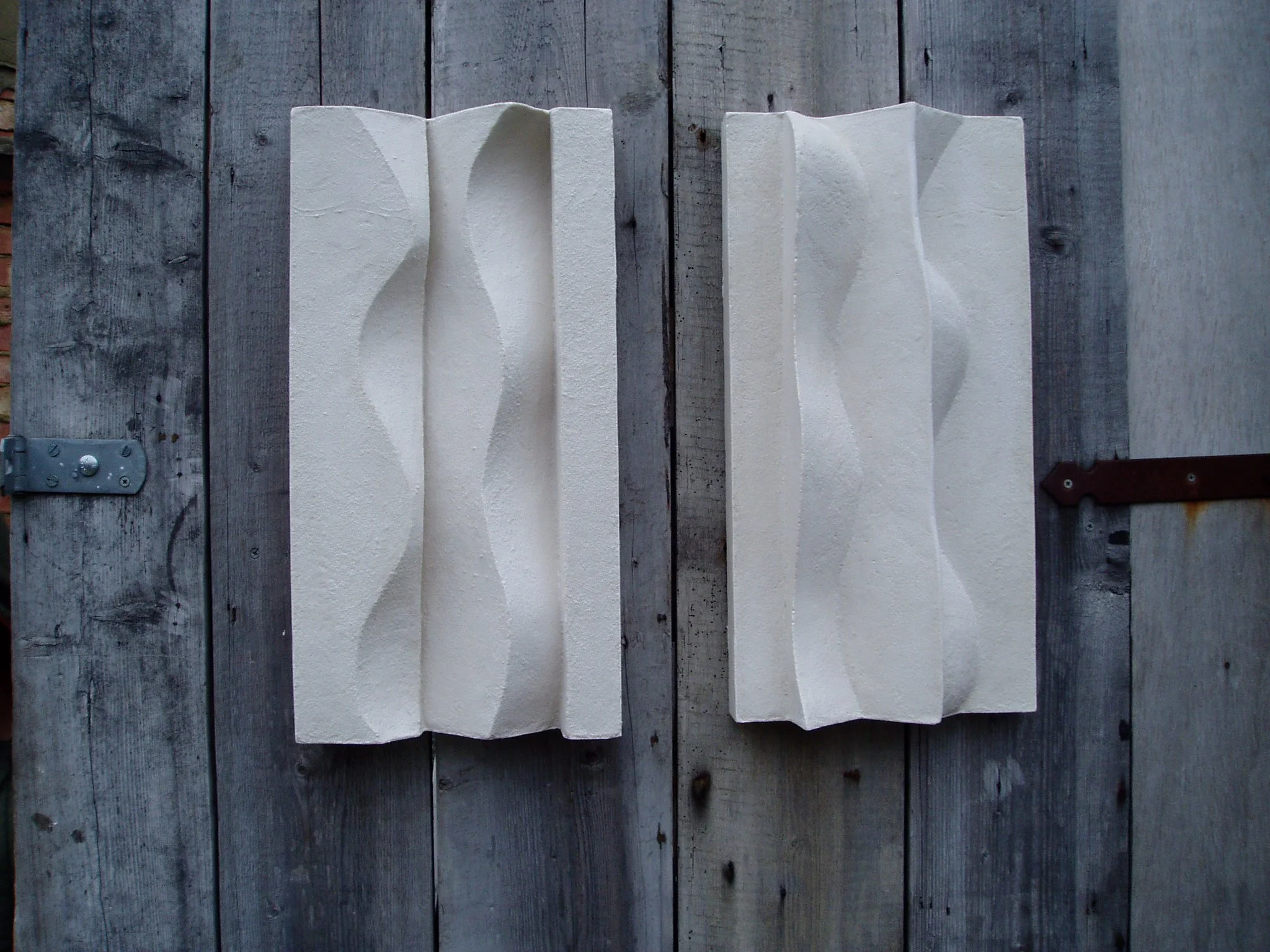 Paired white Brancusi relief panels mounted on a weathered timber door.