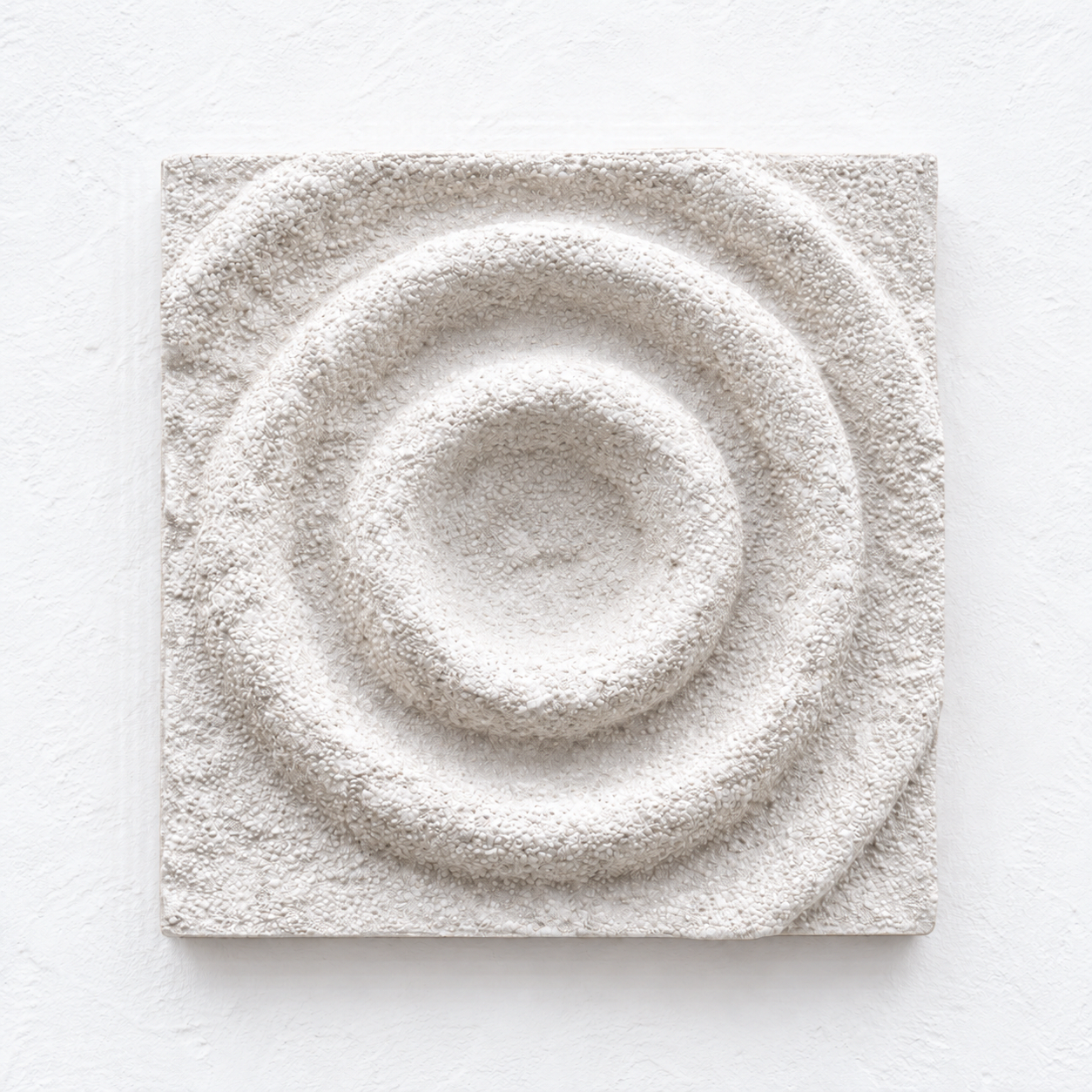 White square Cup Ring relief with a circular central depression and textured concentric rings.