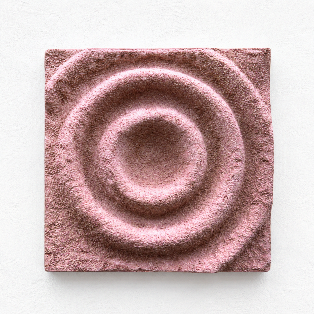 Pink-toned square Cup Ring relief with a recessed centre and raised circular bands.