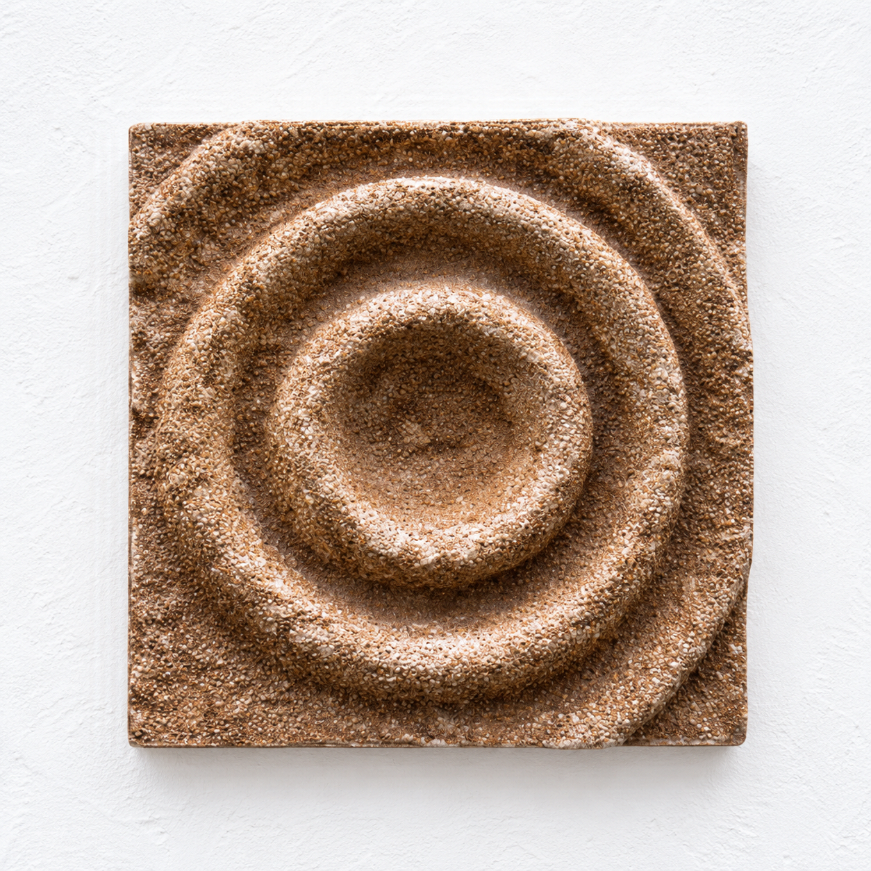 Brown square Cup Ring relief with a circular central depression and raised concentric rings.