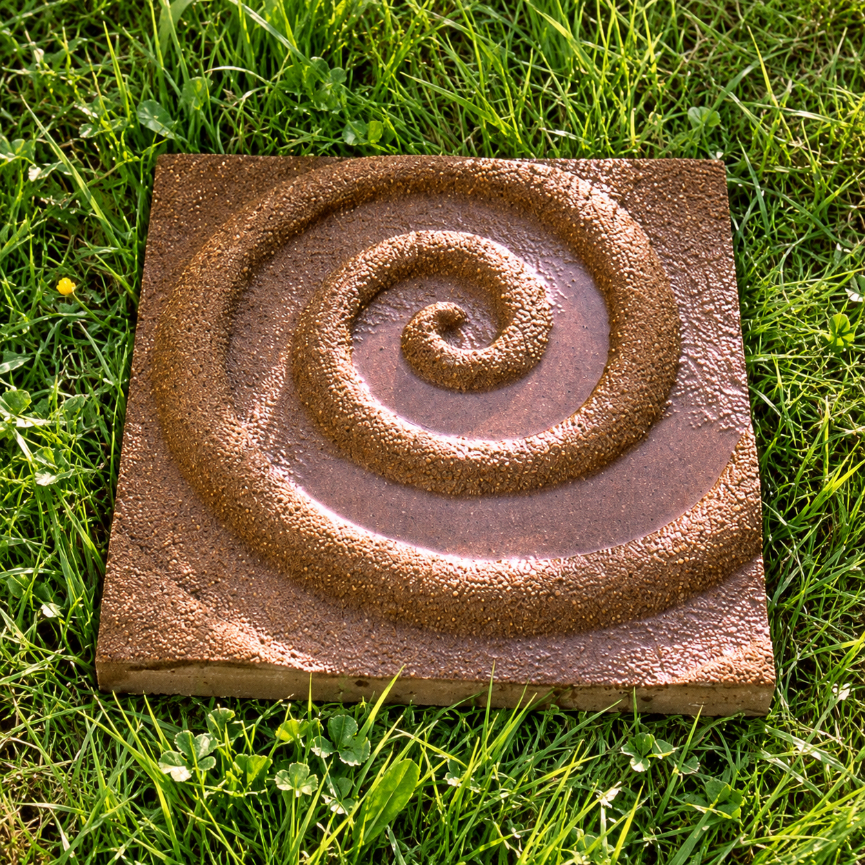 Brown Spiral paver lying on grass, with a raised spiral and rough surface.