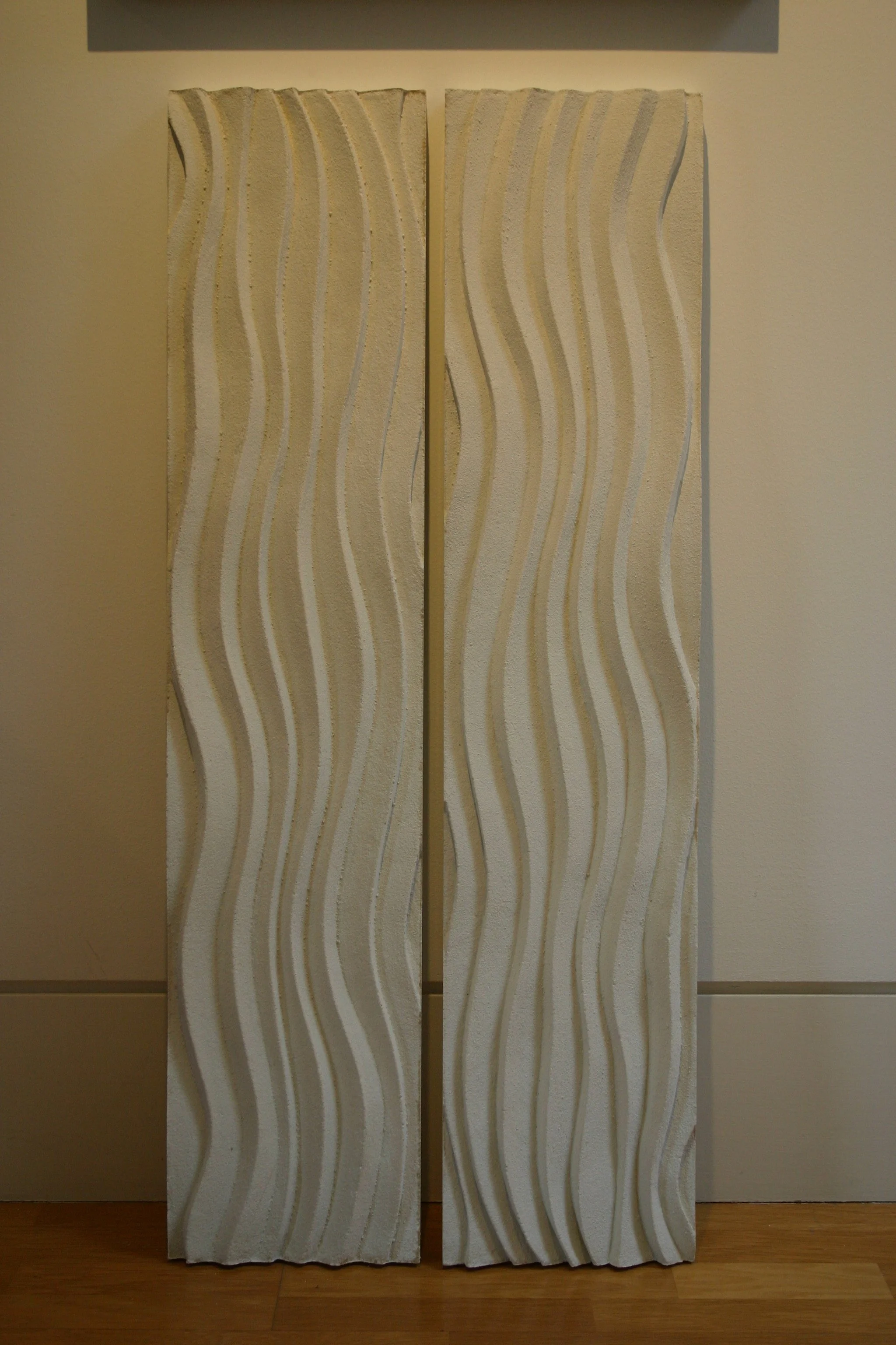 Two tall white wave-pattern relief panels displayed side by side on a timber surface.