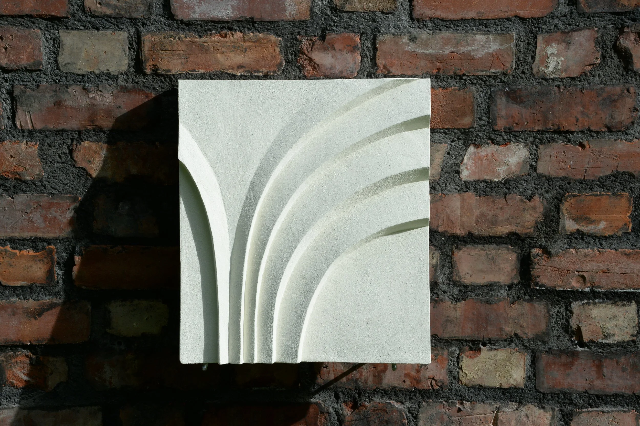 White Deco Palm and Spiral Palm 2 relief mounted on brick, with curved fan-like ridges.