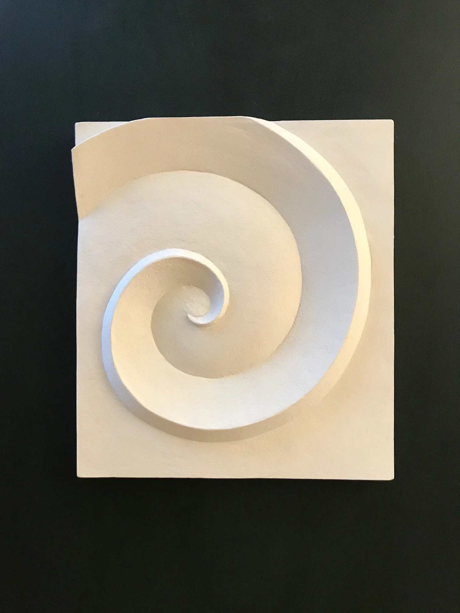 White spiral relief lit warmly against a dark background, showing the depth of its curled centre.