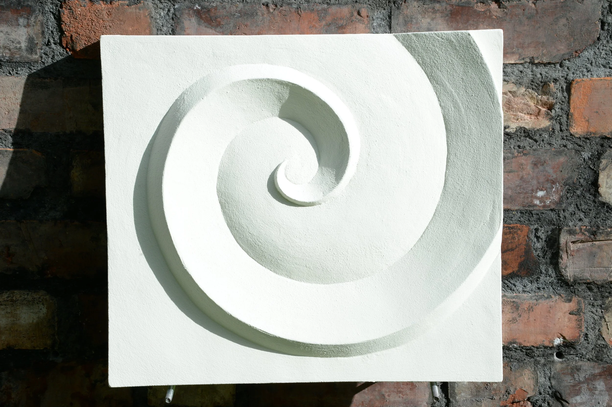 Close view of the white Deco Palm and Spiral Spiral 2 relief on a brick wall.