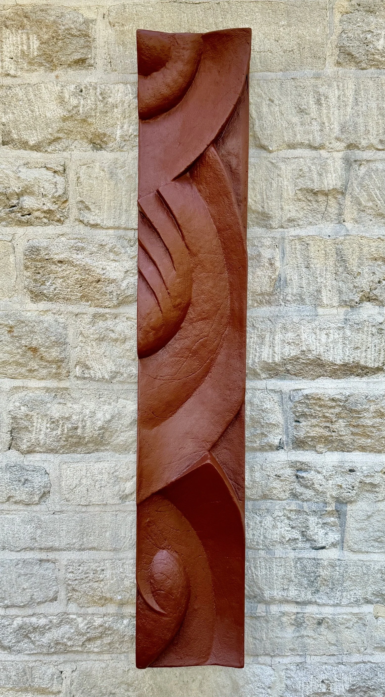 Tall terracotta Decowaves 2 relief with curved bands, fan-like ridges and a spiral on a stone wall.