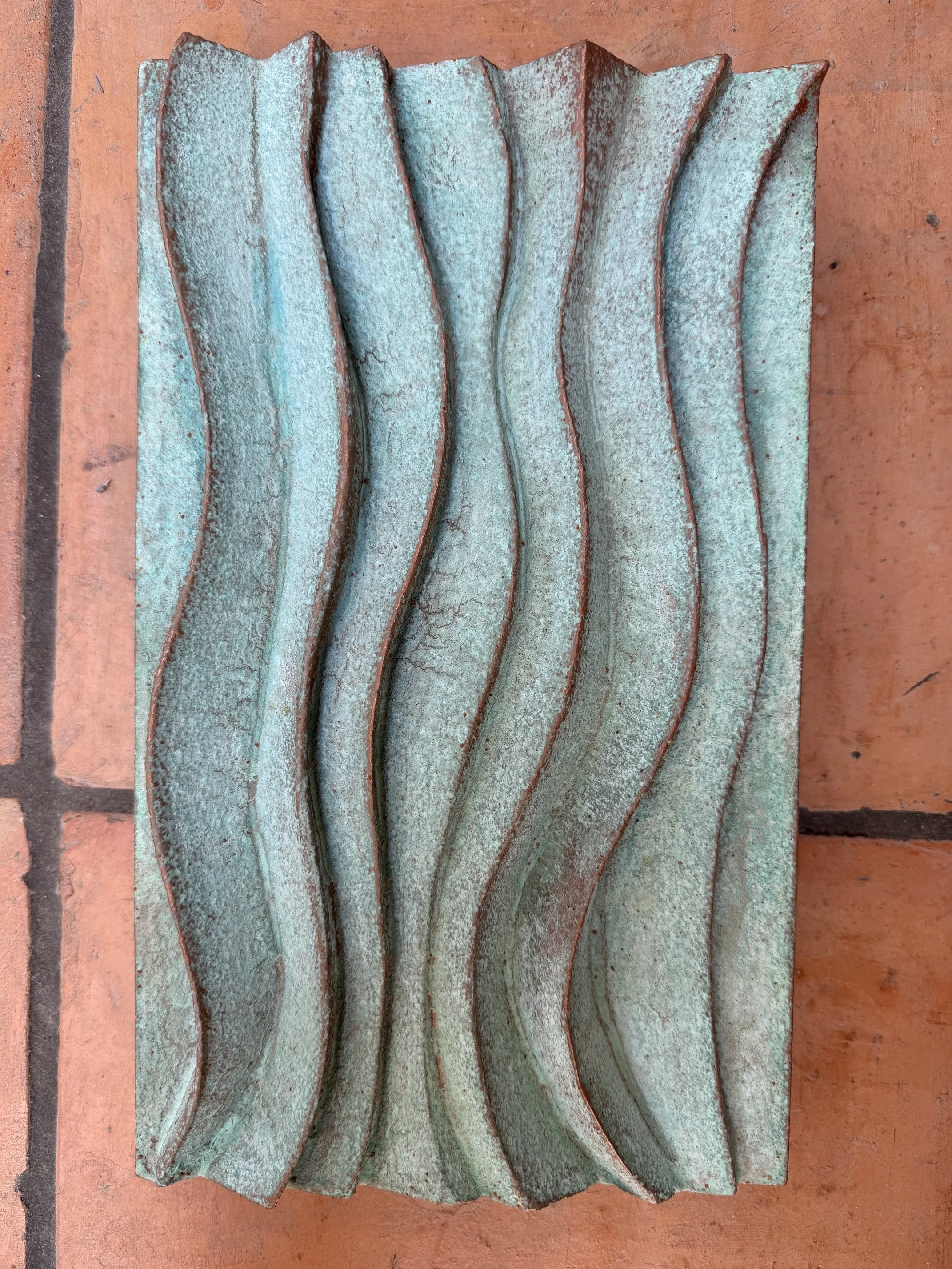 Verdigris Dune Ripple 1 relief with flowing vertical waves, displayed against terracotta tiles.