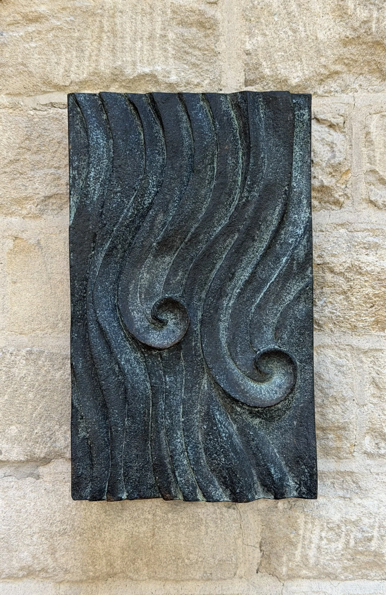 Bronze and verdigris Dune Ripple relief displayed vertically on a stone wall.