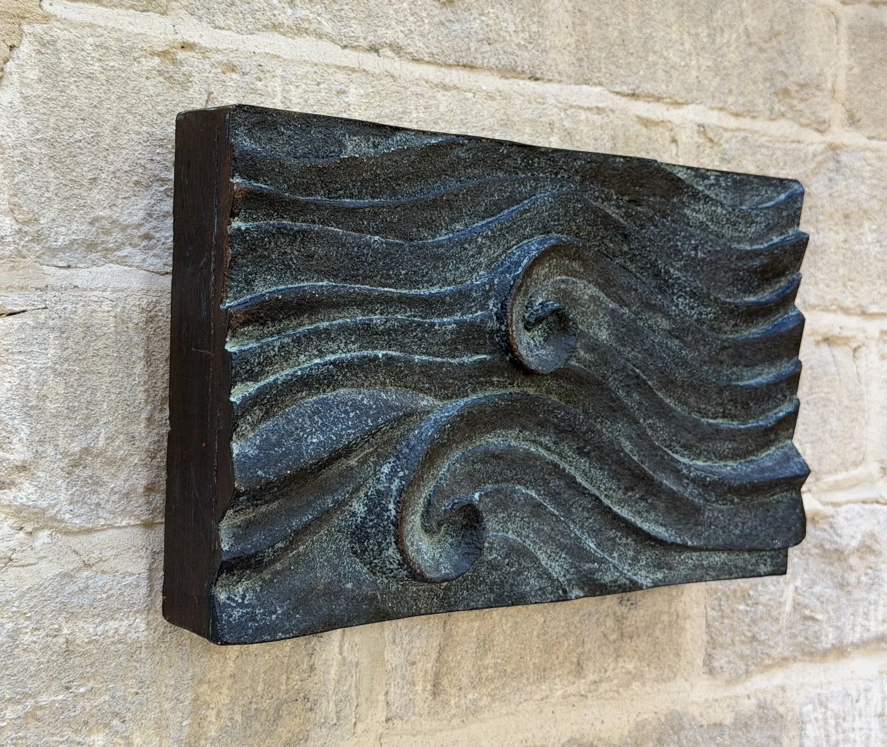 Bronze and verdigris Dune Ripple relief displayed horizontally on stone, showing its projecting ridges.