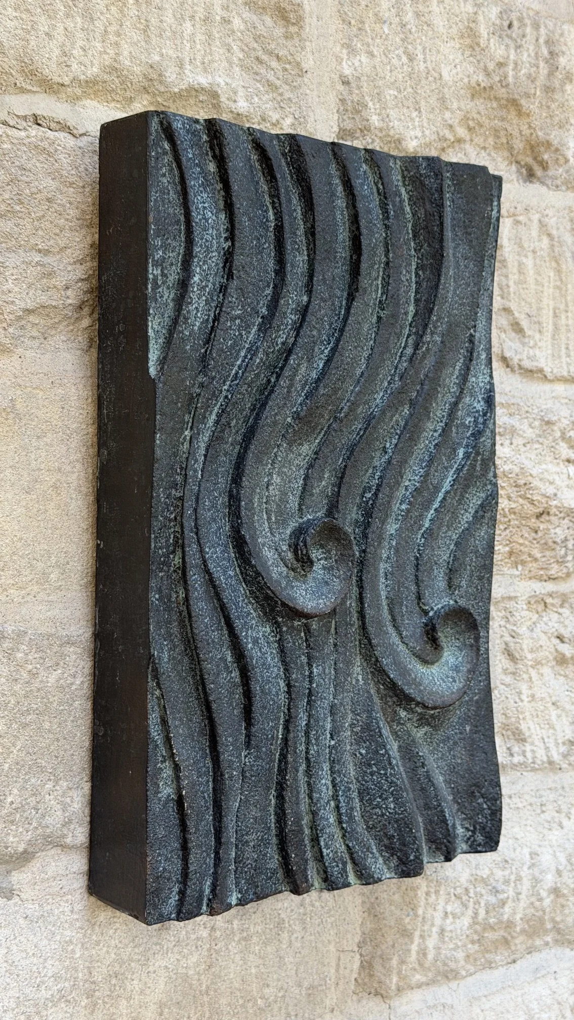 Side view of the bronze and verdigris Dune Ripple relief, showing its depth against stone.