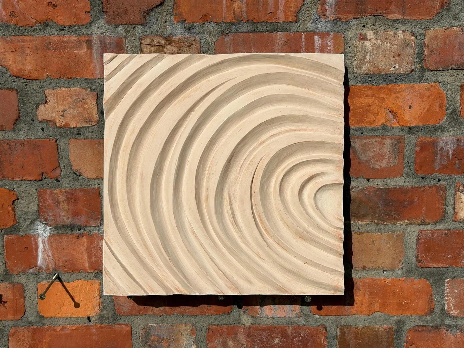 Cream Fingerprint Concentric 2 on brick, with ridges curving towards the right edge.