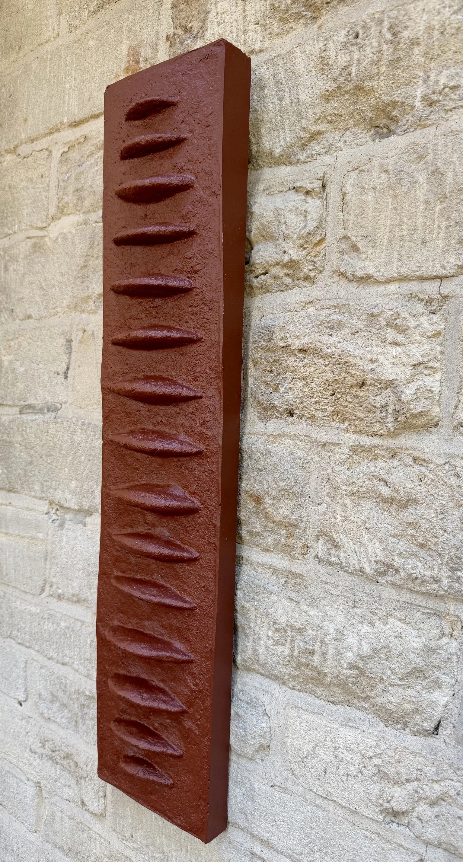 Side view of terracotta Frozen Fish mounted on pale stone.