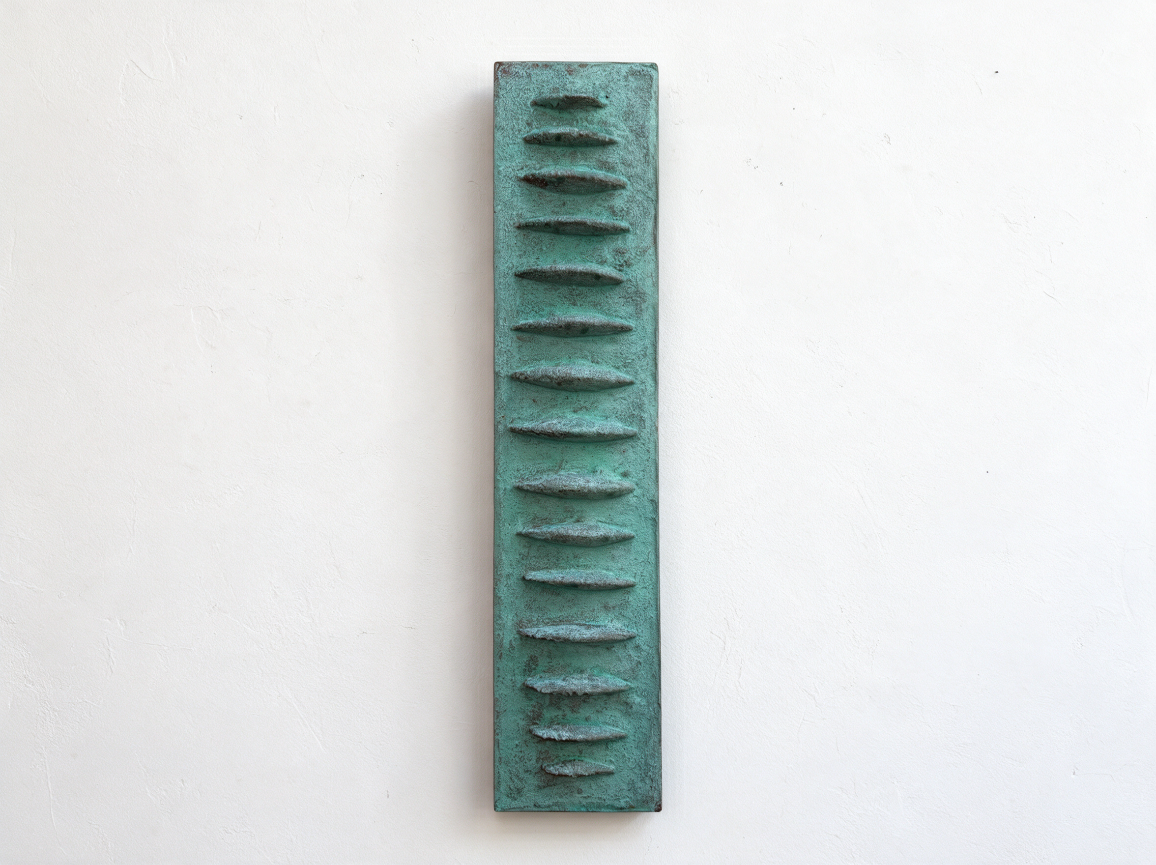Verdigris Frozen Fish with a row of raised tapered forms against white.