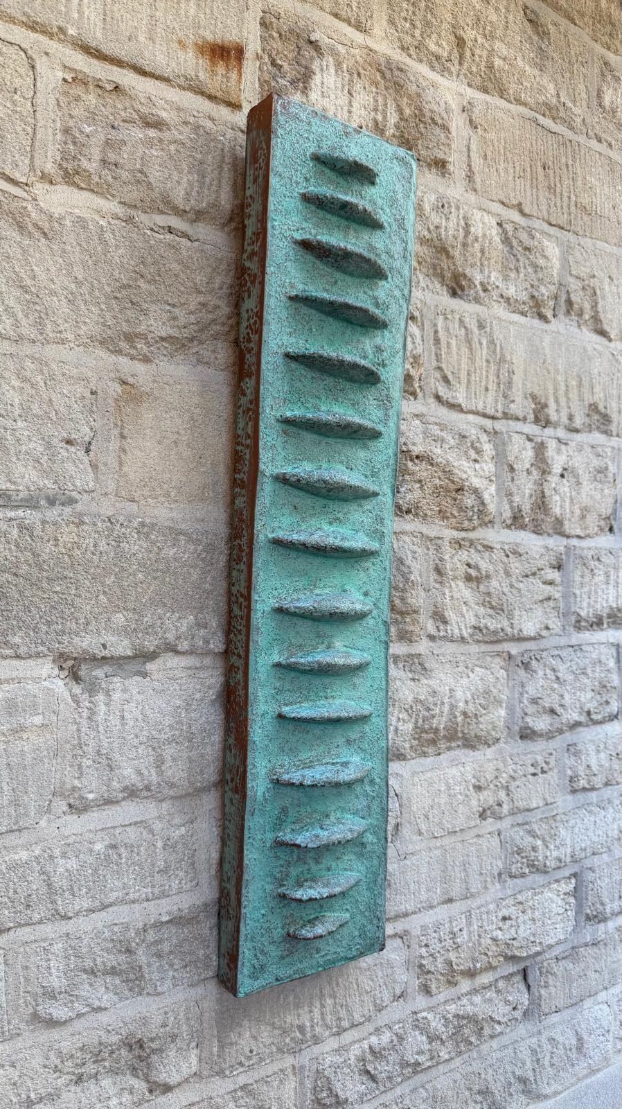 Verdigris Frozen Fish with repeated fin-like shapes, shown at an angle on stone.