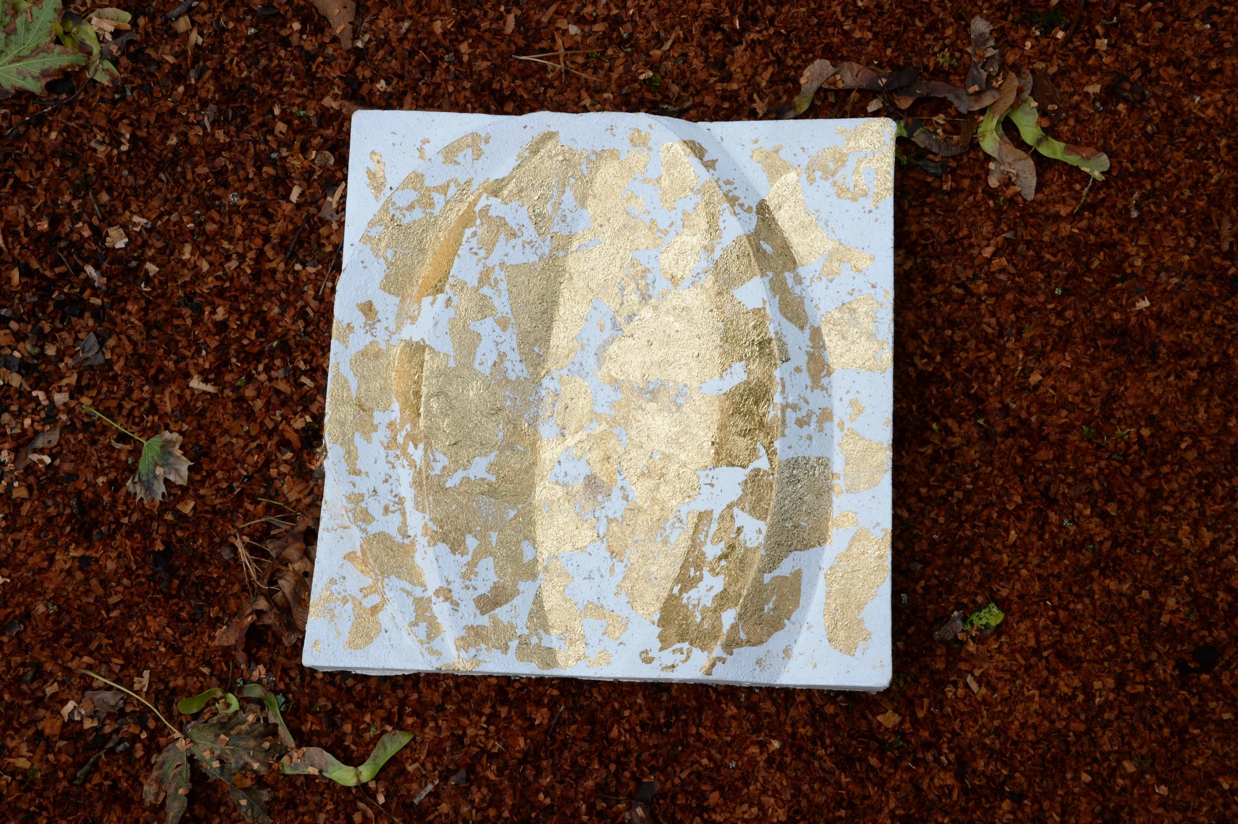 White and gold-coloured Leaf Curve relief shown on a rough outdoor surface.