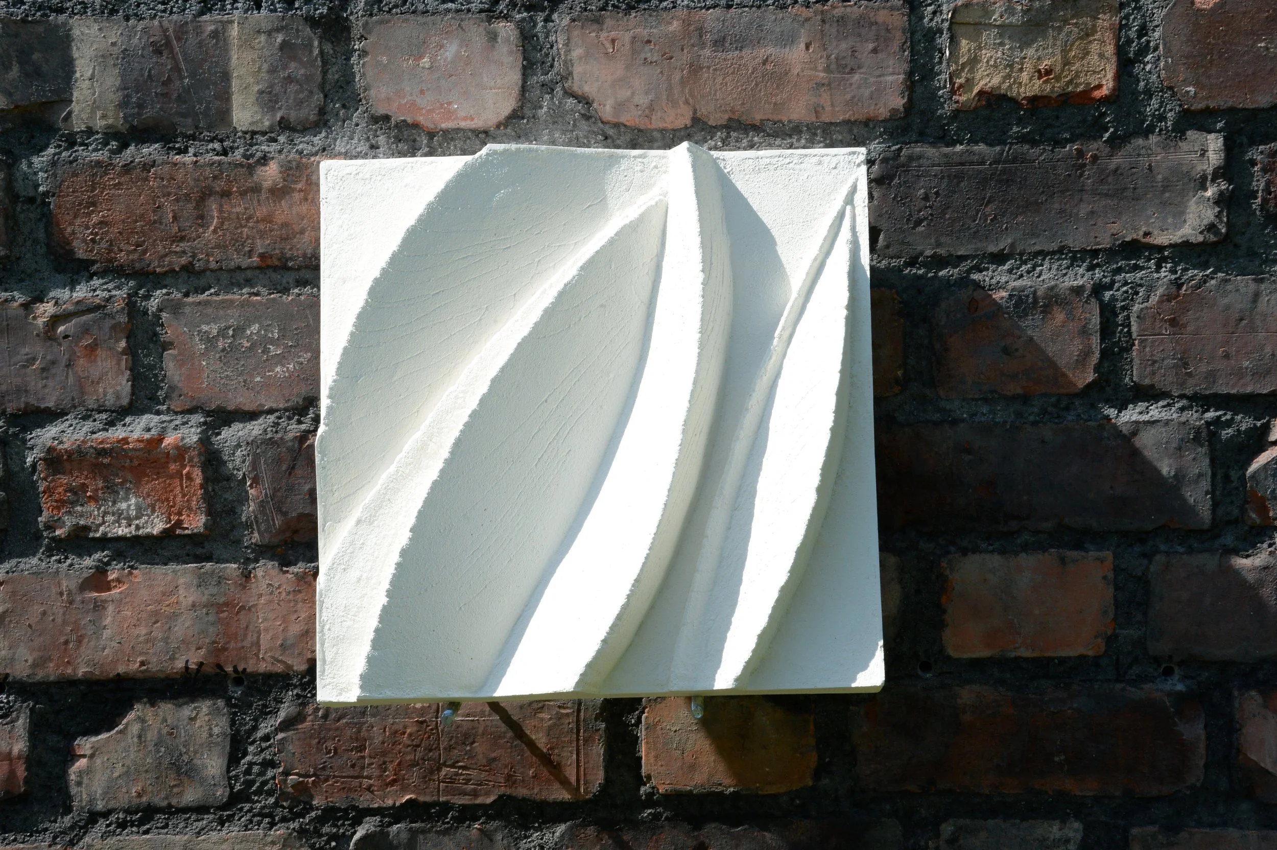 White Leaf Form 1 with raised leaf-like curves on a brick wall.