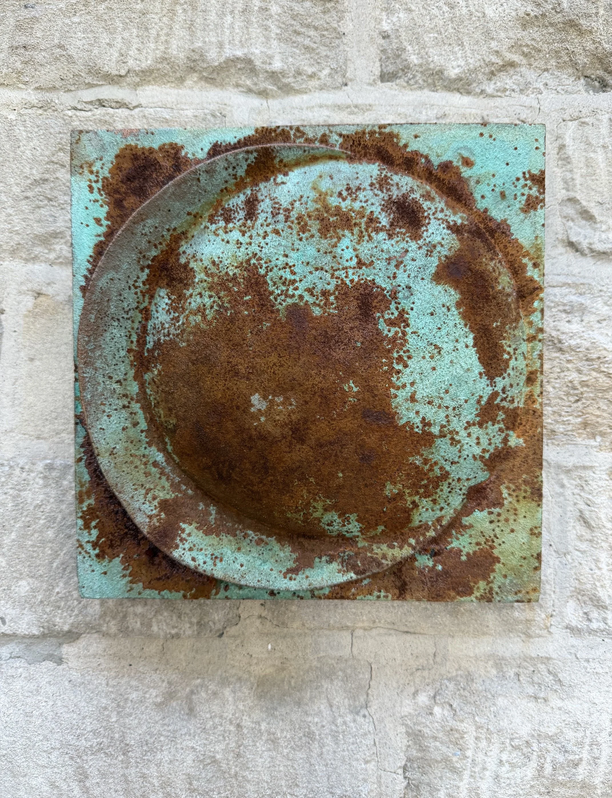 Verdigris and rust Moon Crater Phase 1 relief with a raised central disc, mounted on stone.