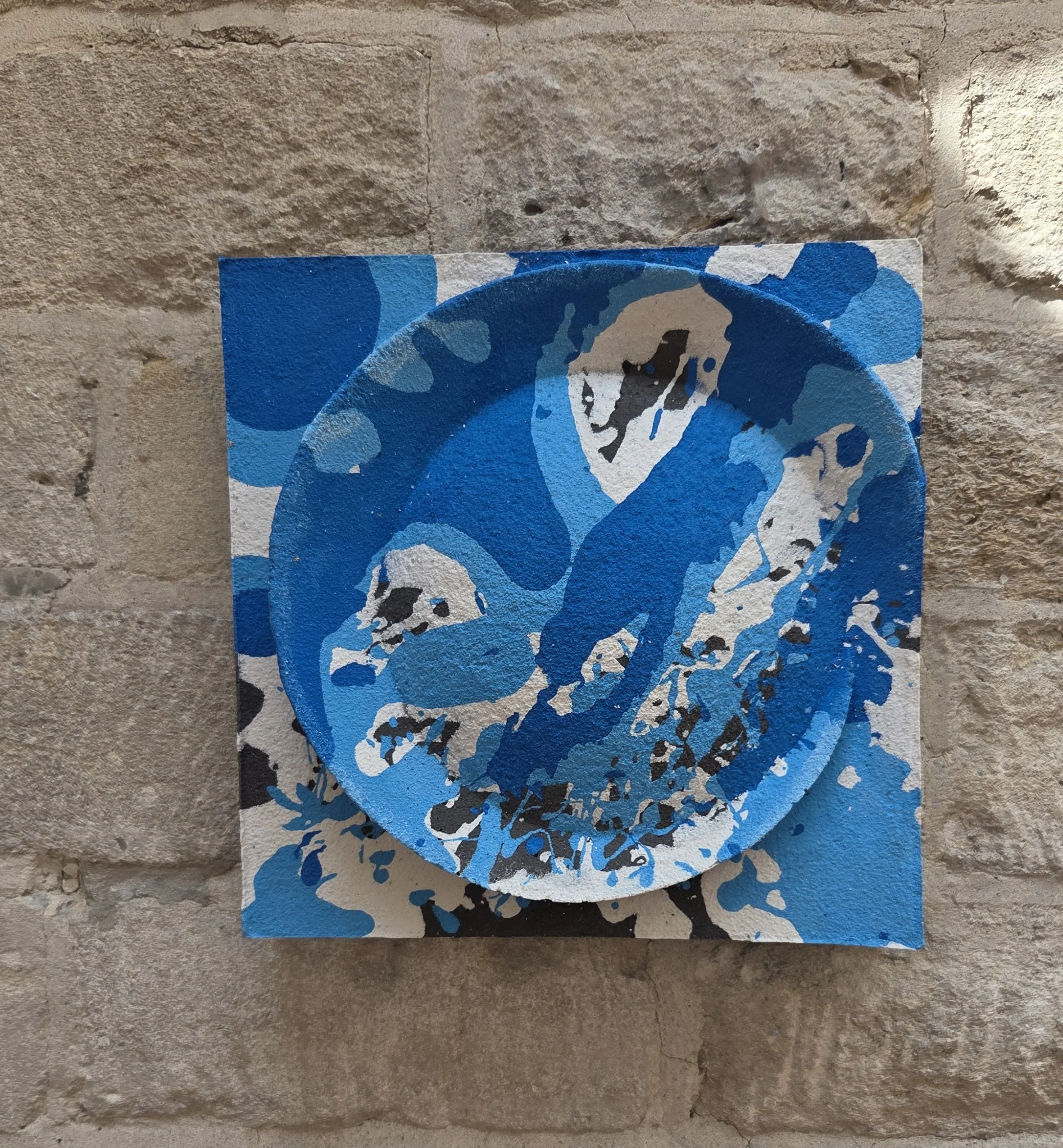 Moon Crater Phase 2 with blue, white and dark splashes, displayed on a stone wall.