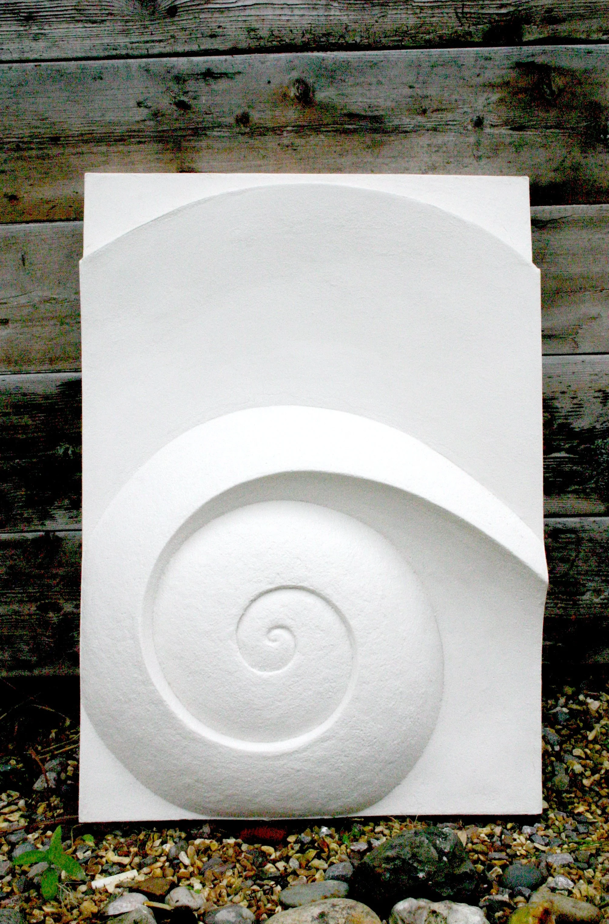 White Moonspiral 2 relief photographed outdoors beside timber and foliage.