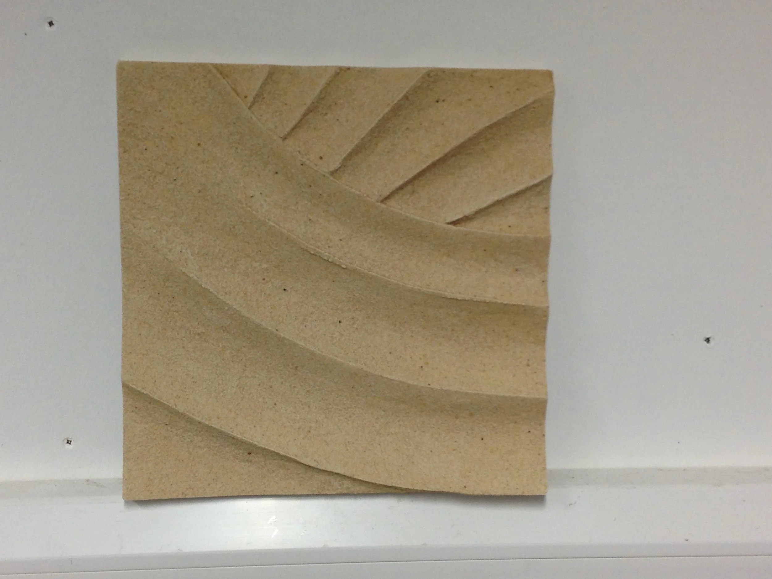 Beige Panel Curves relief with sweeping bands and short diagonal marks, resting on a ledge.
