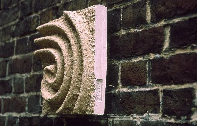 Angled view of the beige Raked Spiral 3 textured spiral panel on a brick wall.