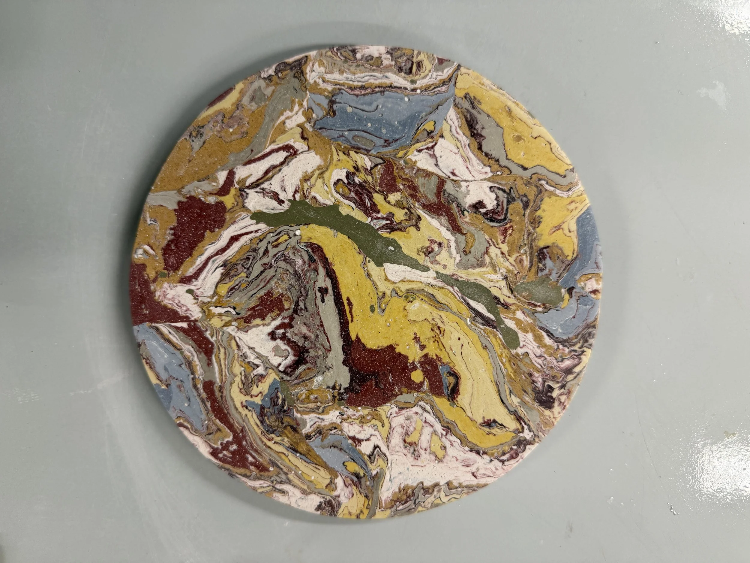 Circular marbled wall panel with yellow, cream, brown and grey swirls, photographed against a grey surface.