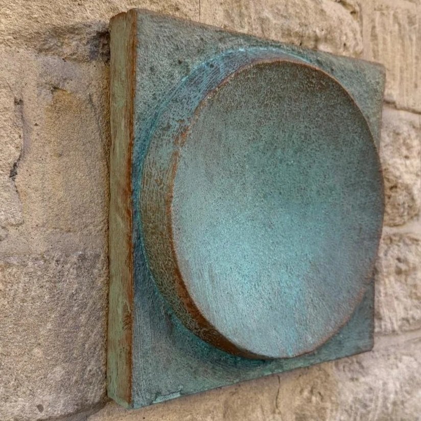 Spherical Verdigris wall sculpture viewed from the side, the verdigris dome projecting from its panel on a stone wall