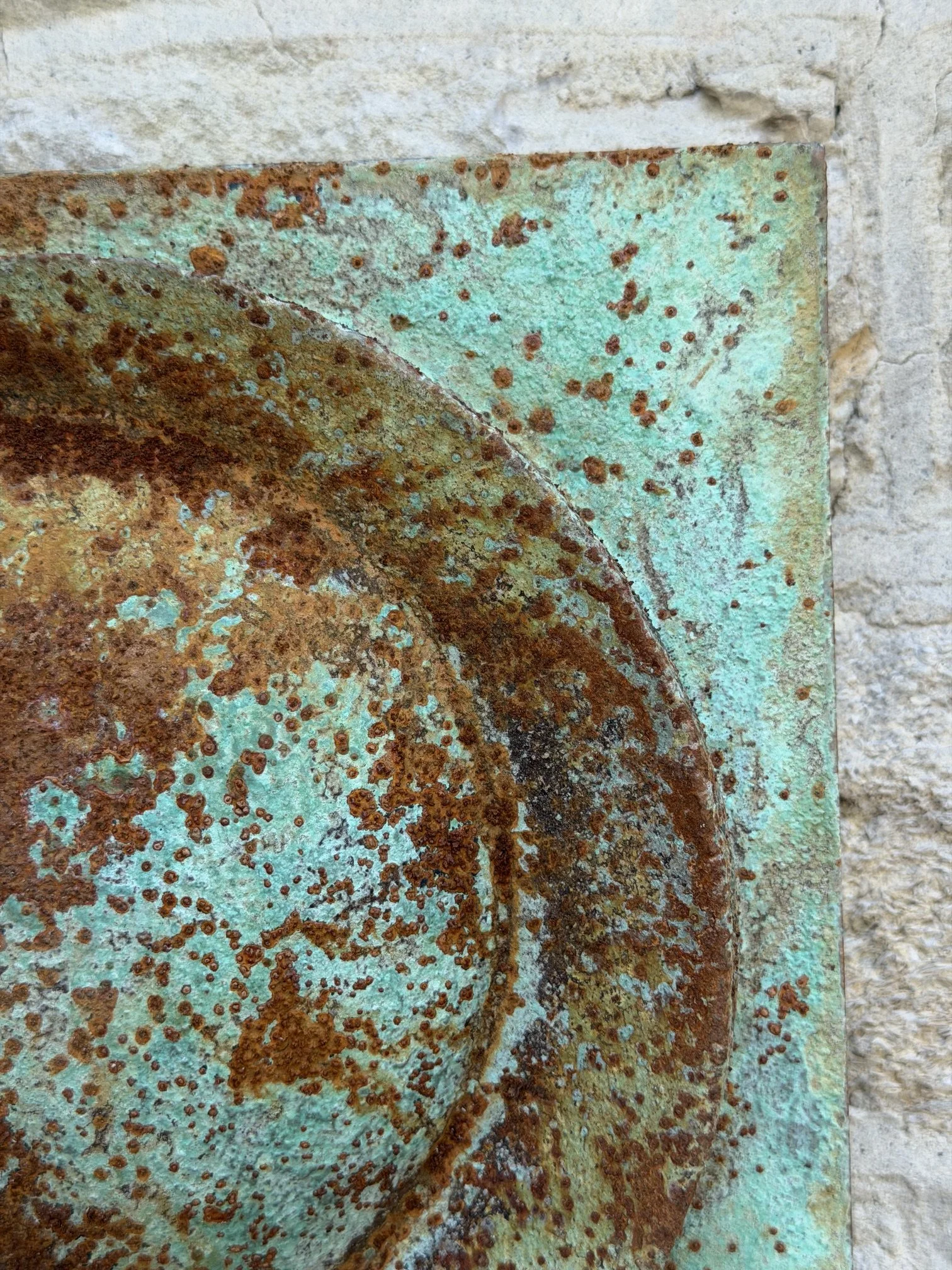 Moon Crater Phase Verdigris Spherical Wall Sculpture seen at an angle against a stone wall