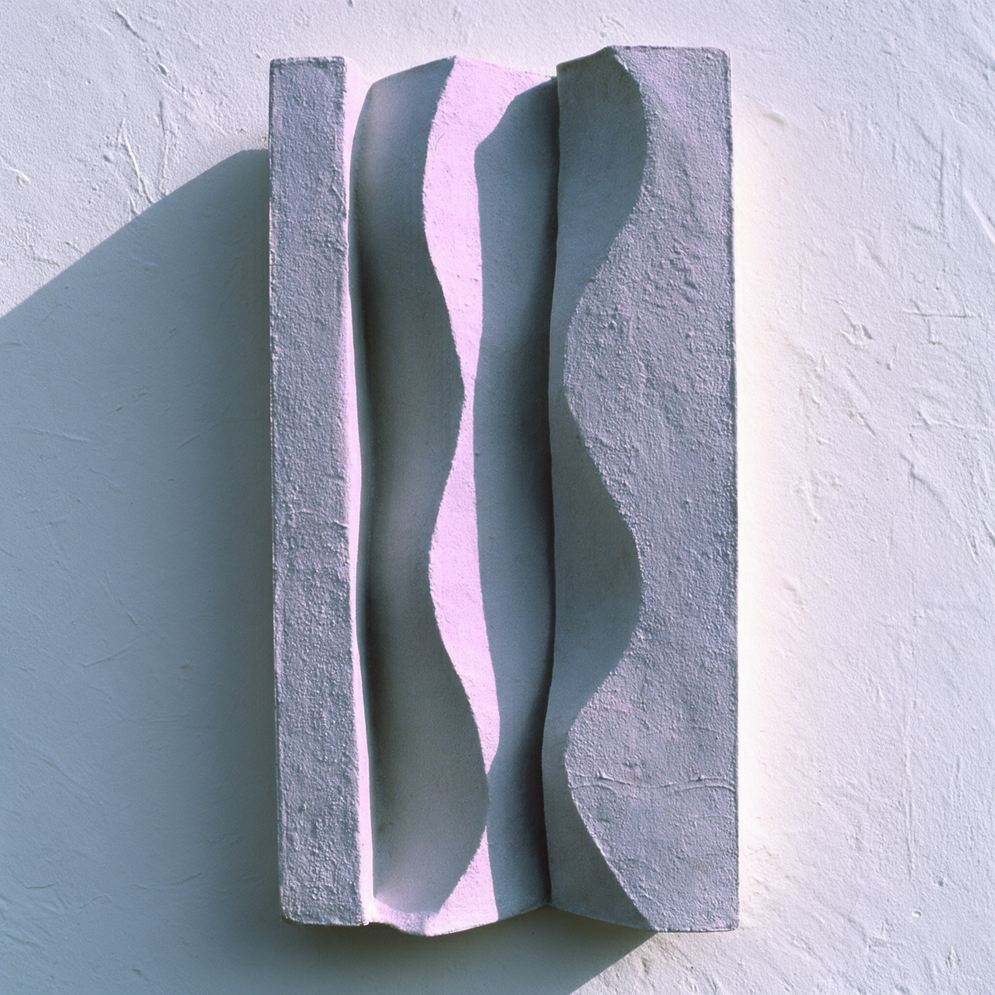 White Brancusi 1 relief in strong sunlight, casting a shadow across a pale wall.