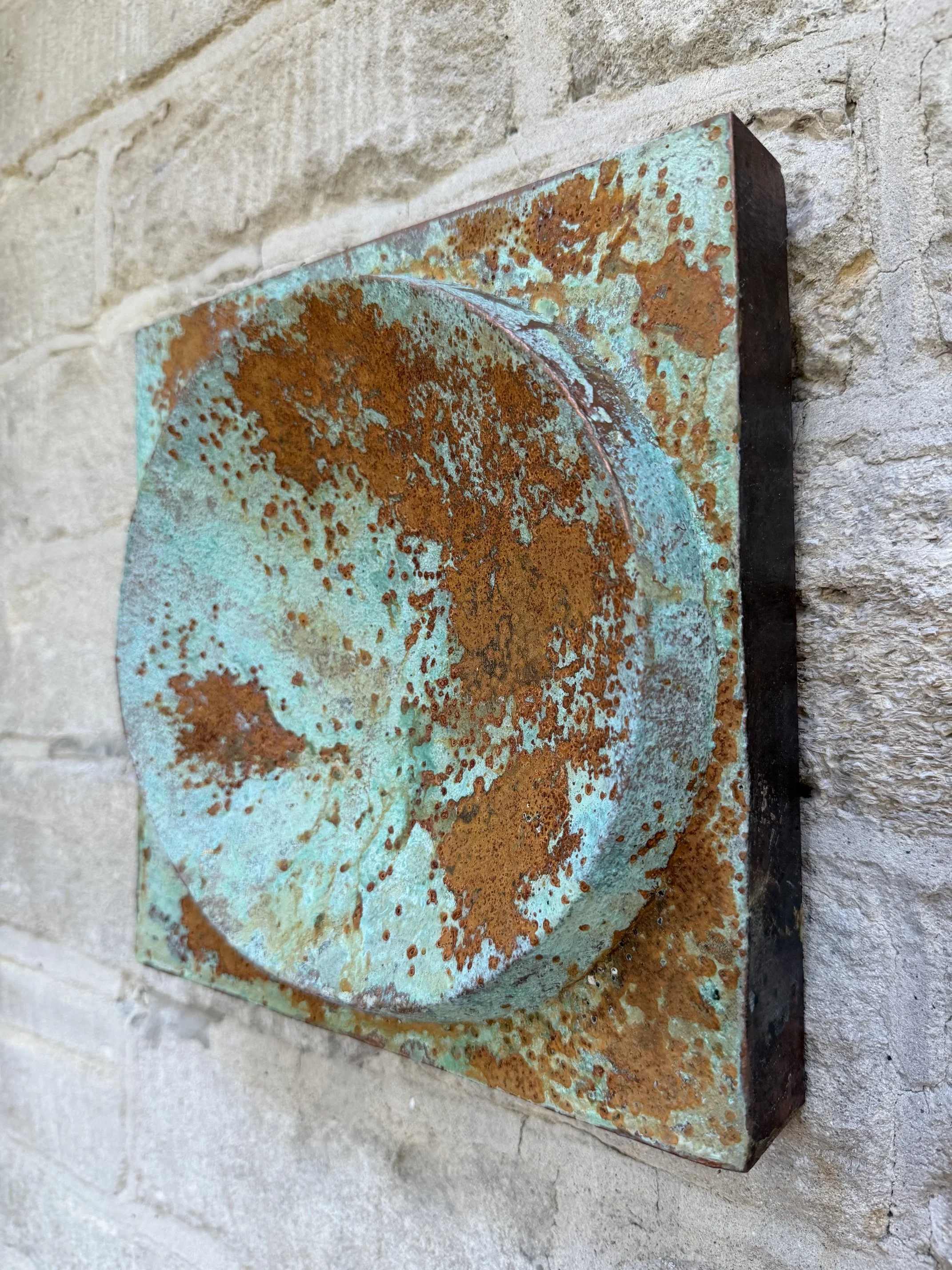 Moon Crater Phase Copper Verdigris Wall Sculpture at a three quarter angle against pale stone