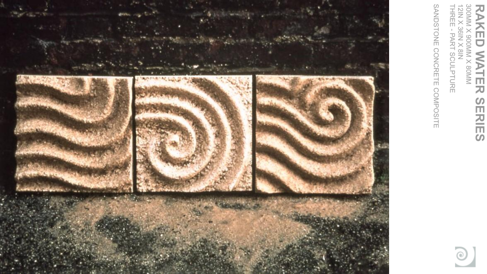 Three carved sandstone blocks with swirling spiral designs, placed on a dark surface with scattered sand.