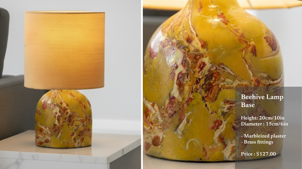 A beige lampshade sits on top of a yellow and red marbled plaster lamp base on a white table, with a grey couch partially visible to the left.