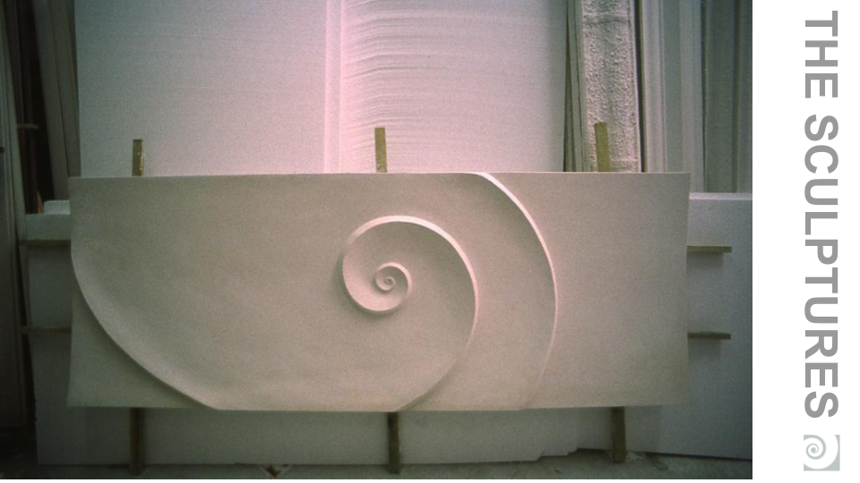 A large sculpture of a spiral shell design in a workshop or studio space.