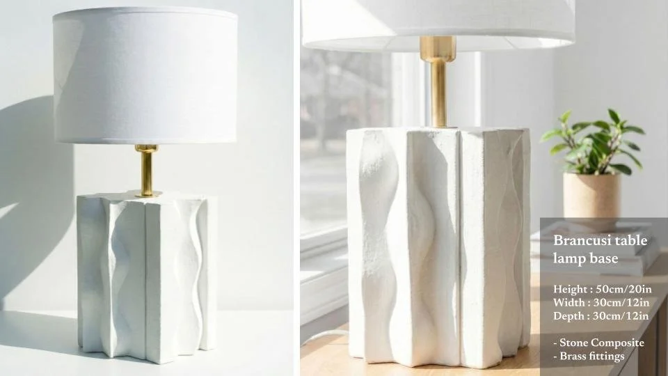 A white table lamp with a stone composite base and brass fittings, placed on a table near a window with sunlight.
