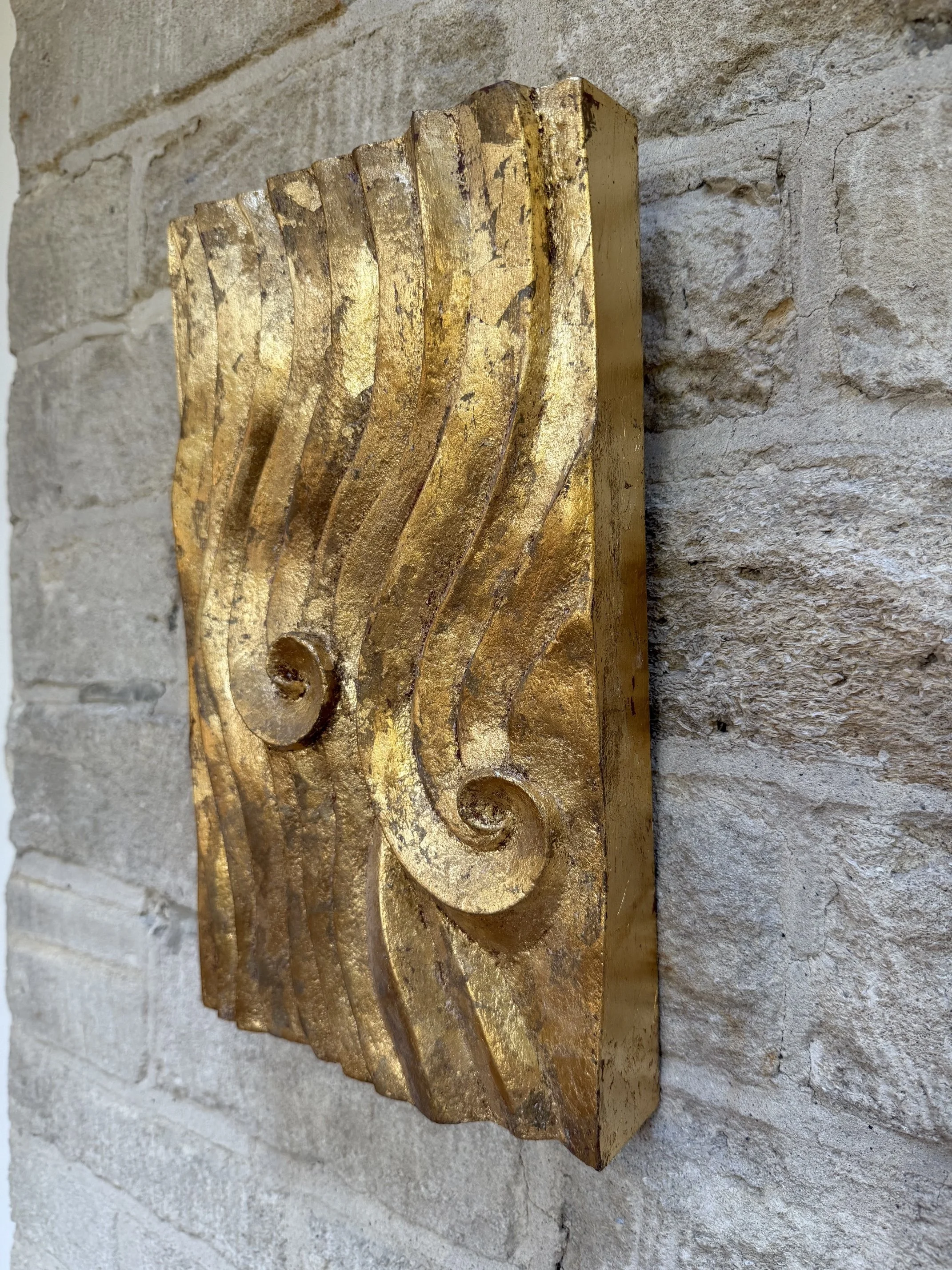 Gold-Leaf Wave Relief Sculpture in profile against a stone wall, showing the depth of the carving