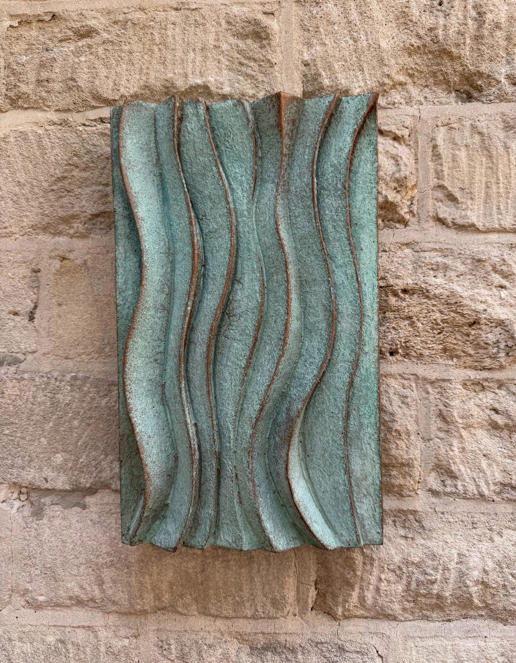 Verdigris Ripple Wave Wall Sculpture, a panel of vertical rippling waves in green verdigris on stone