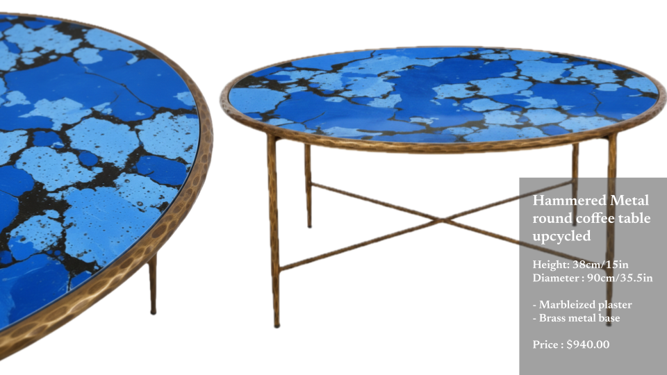 A distressed metal round coffee table with a blue and black marbleized plaster top and a brass metal base.