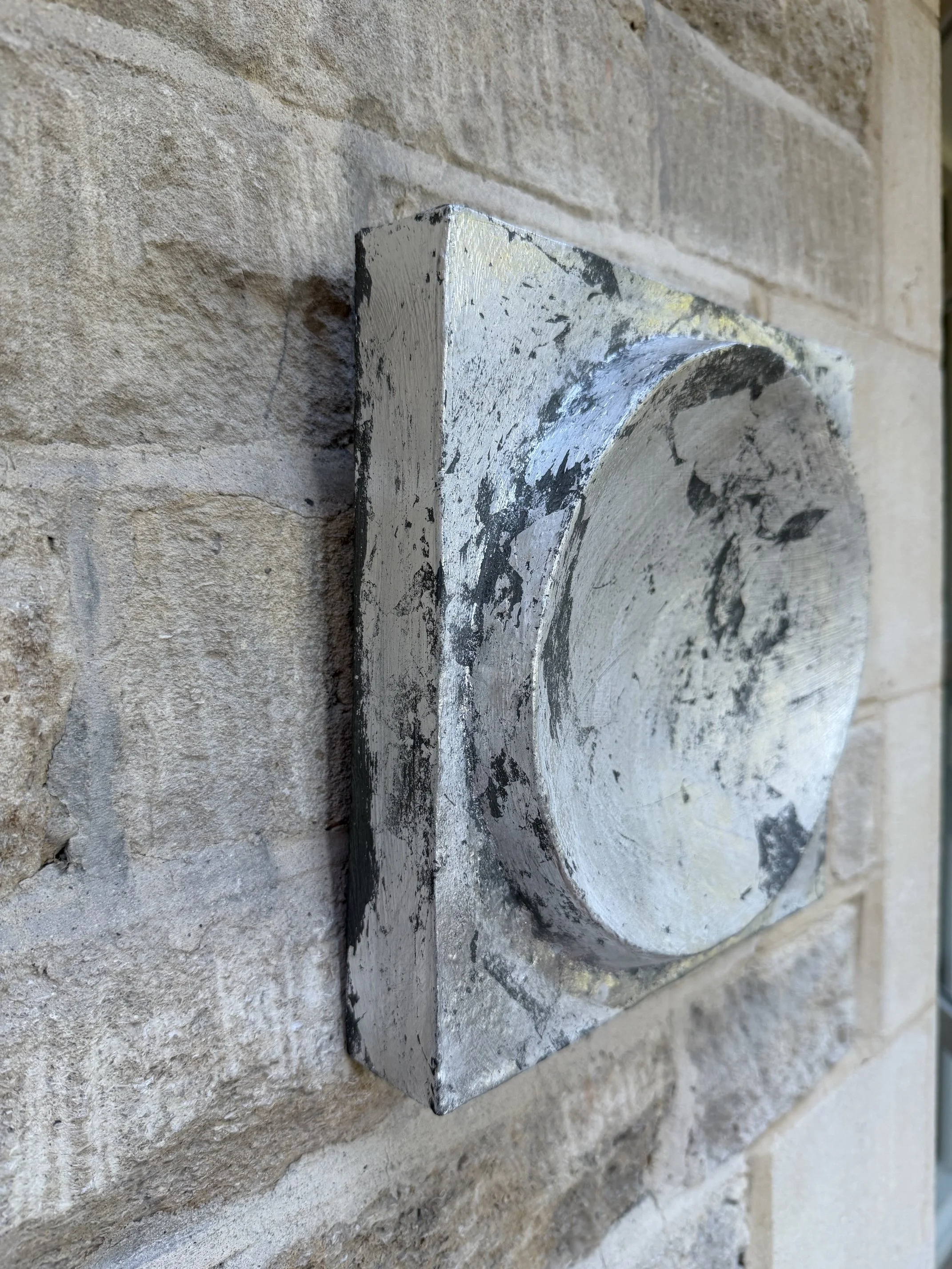 Silver and Bronze on Concave Moon viewed from the side against a stone wall