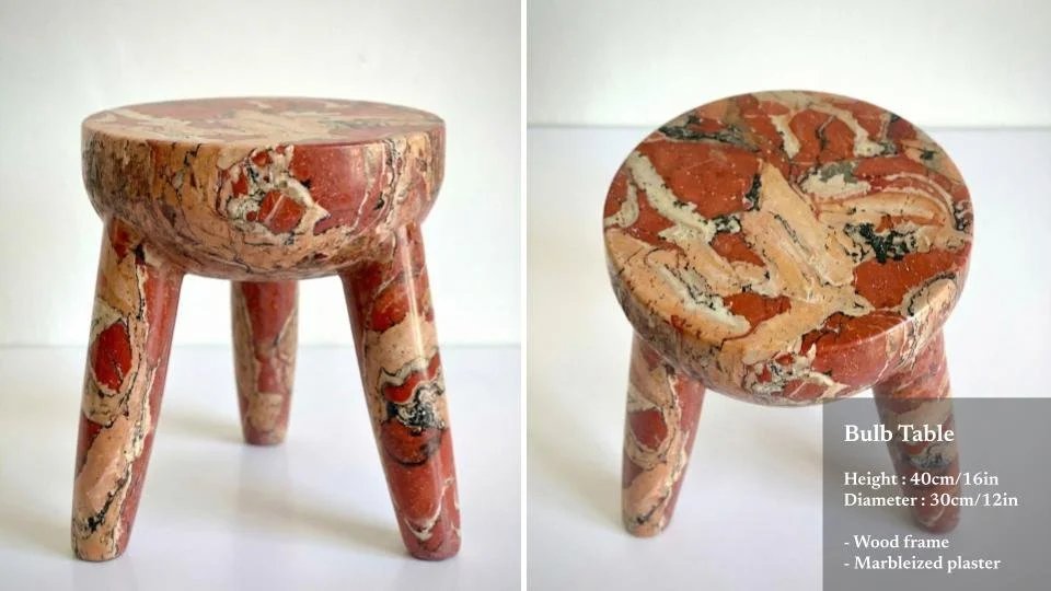 Small stool made of marbleized plaster with three angled legs and a round top, featuring red, beige, and black marbling patterns.