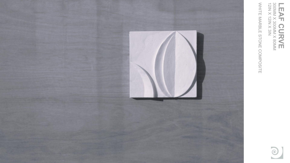 Square white marble or stone tile with carved curved leaf or petal design, placed on a light gray wooden surface.