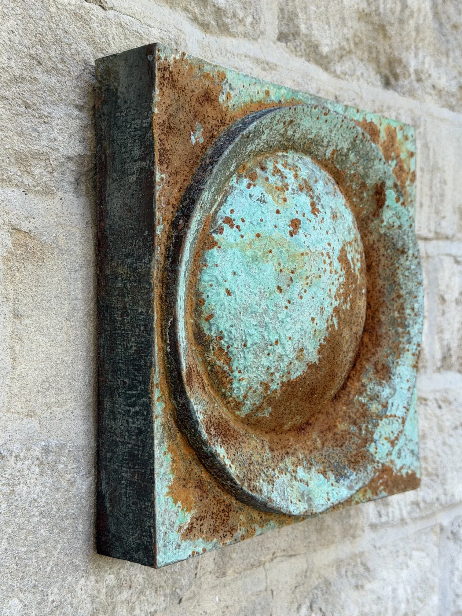 Moon Crater Verdigris Rust Wall Sculpture seen at an angle against a stone wall